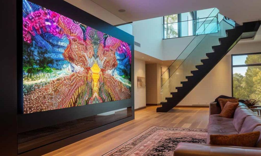 Modern living room with a large, vibrant video wall, sleek staircase with glass railing, and cozy seating area.
