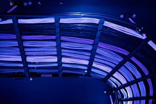 A neatly organized array of cables arranged in an overhead tray, illuminated by soft purple and blue lighting.