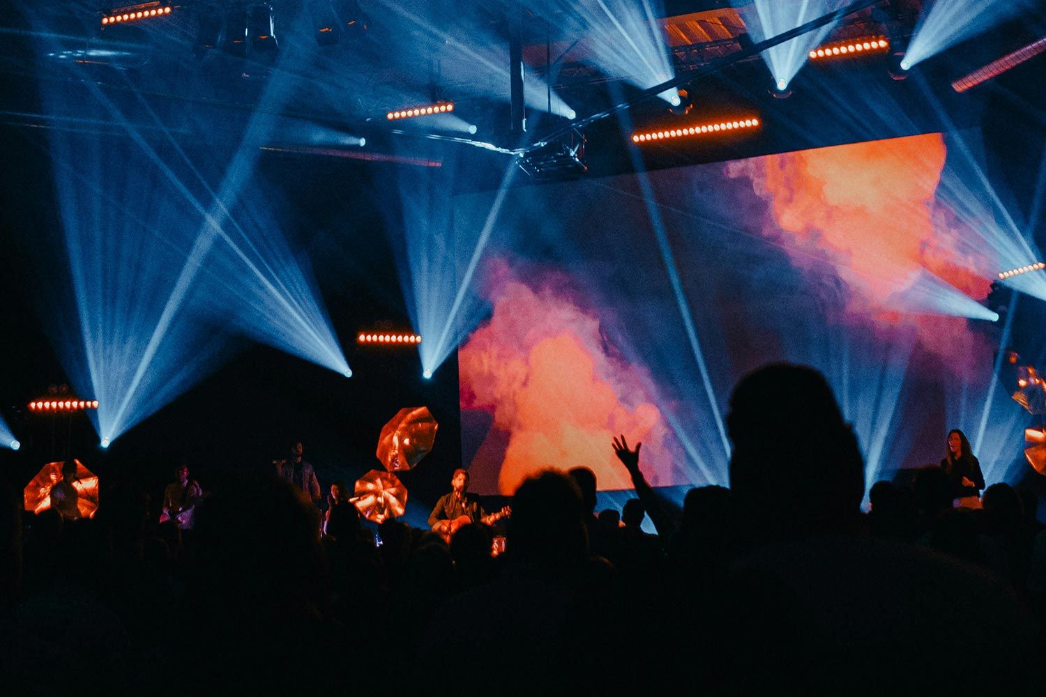 A vibrant house of worship stage with musicians performing in front of a large video wall displaying colorful visuals, enhanced by dramatic lighting effects.