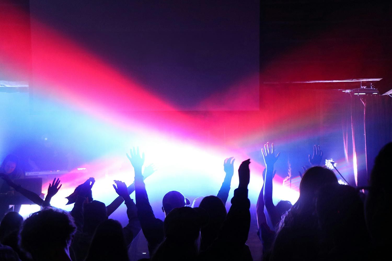 Congregation members with raised hands, illuminated by bright, multicolored stage lights during a dynamic worship session.