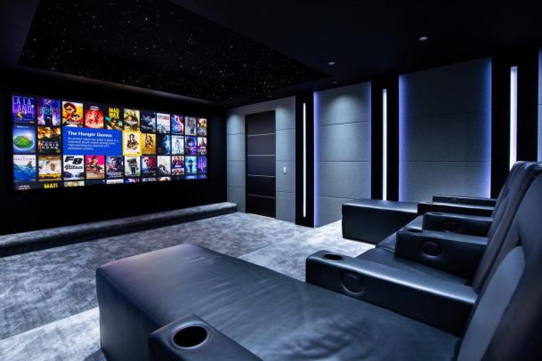 A luxurious home theater with black leather recliners, a large screen displaying movie covers, and a starry ceiling with subtle LED lighting.