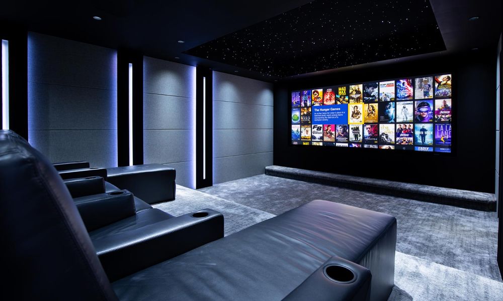 Luxurious home theater with a large screen displaying movie covers, black leather recliners, and ambient blue lighting.