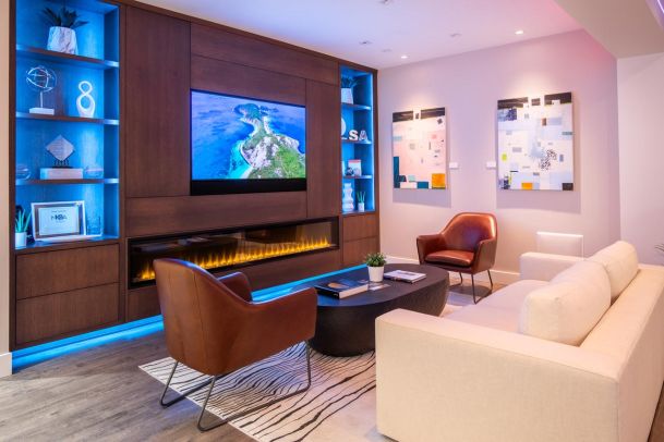 A cozy living area with a wall-mounted TV, an electric fireplace, and a seating arrangement with a sofa and accent chairs, complemented by decorative shelving.